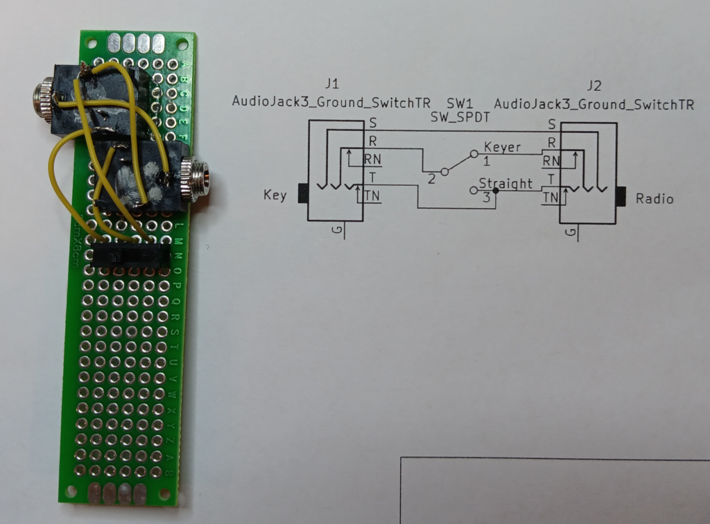 A photo of a PCB breadboard with some 3.5 mm sockets glued on, wired to each other and sharing connections with a SPDT switch. The thing is sitting on top of a printout of the schematic of the thing.