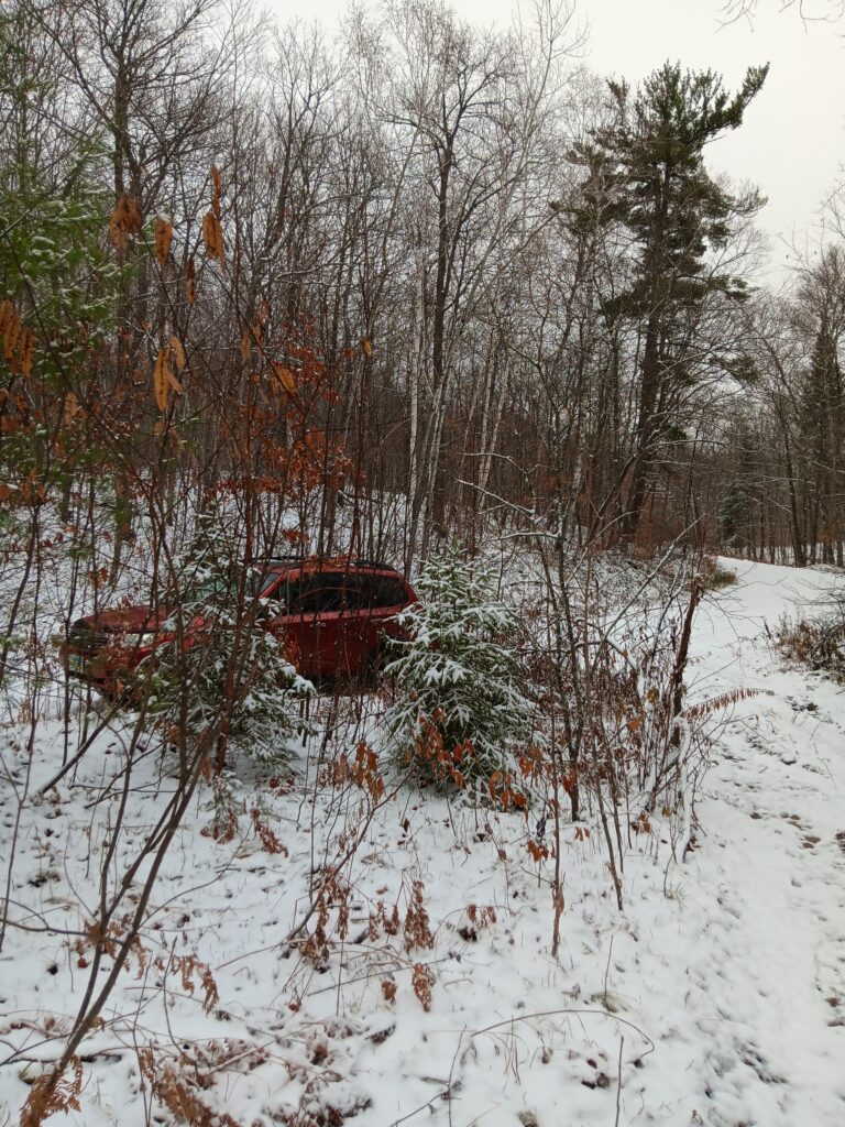 Photo of some snowy Minnesota woods with a red Subaru Forester tucked off a dirt road. The two-track I climbed starts on the right. No sun, just clouds.