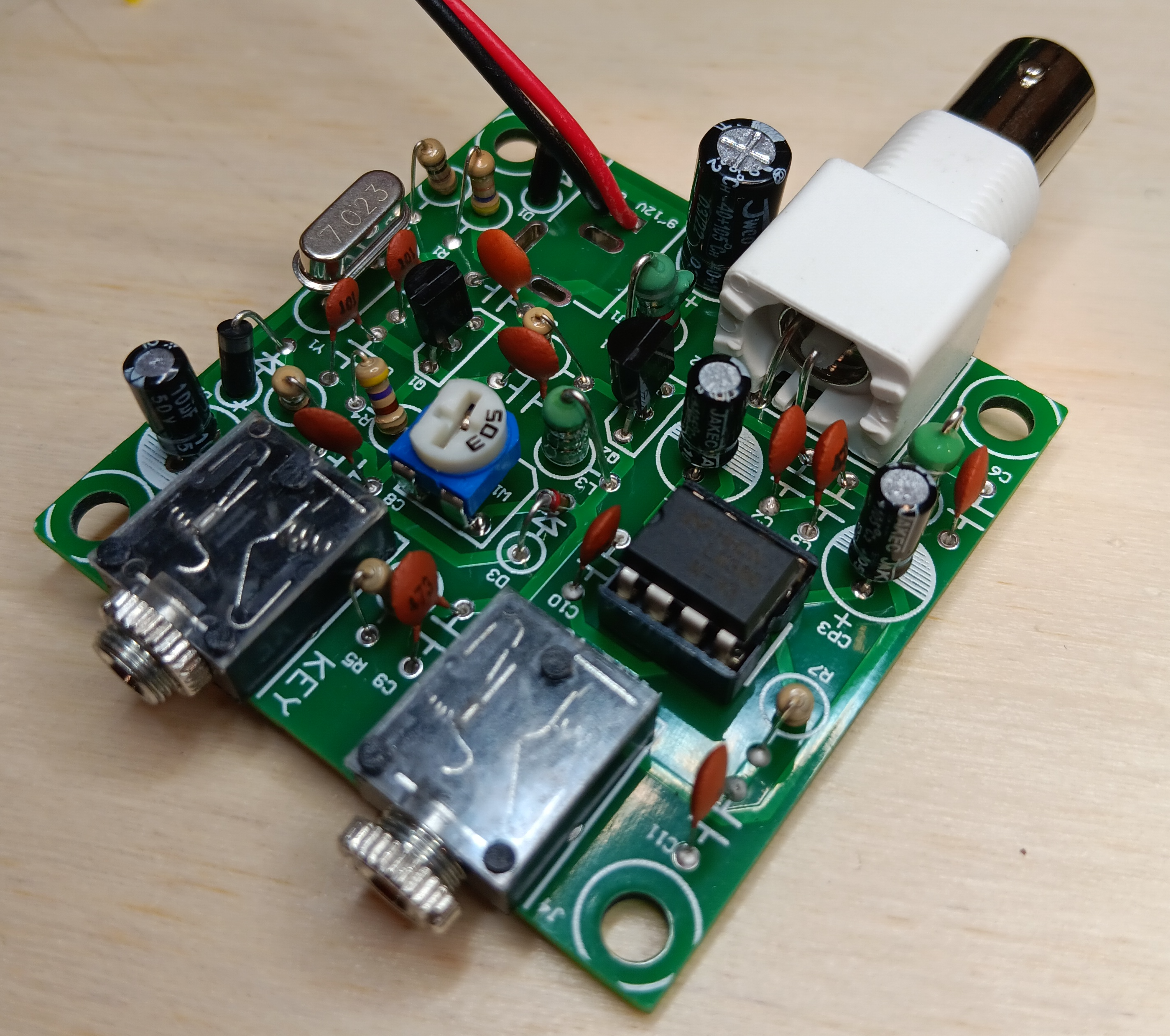 Photo of a Pixie transceiver kit that I assembled. Lots of through-hole parts on a small circuit board. I replaced the supplied barrel power connector with a 9V battery connector that you can't see the end of.